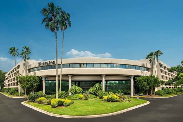 Sheraton hotel exterior with curved facade, palm trees, and manicured landscaping