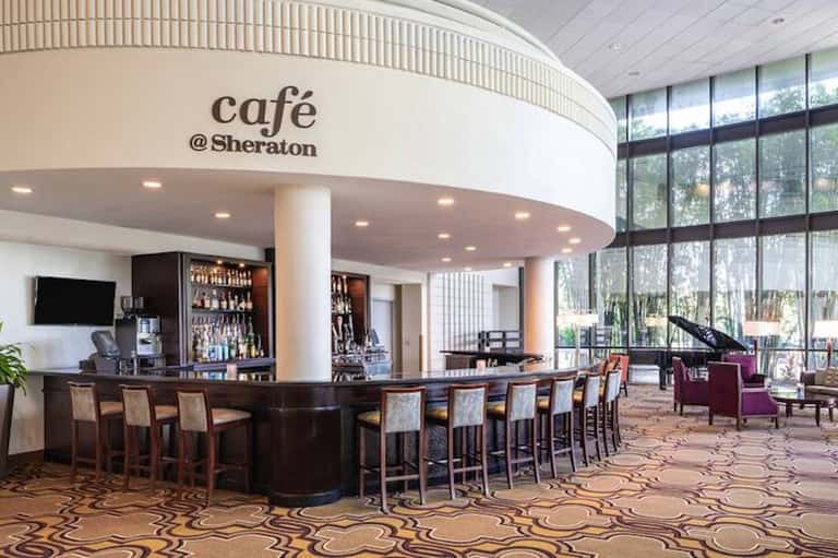 Modern café at Sheraton with curved bar counter, high seating, floor-to-ceiling windows overlooking grounds