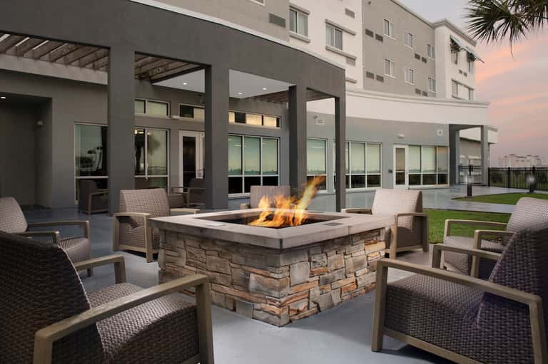 Outdoor fire pit seating area with gray woven chairs and modern building facade at dusk