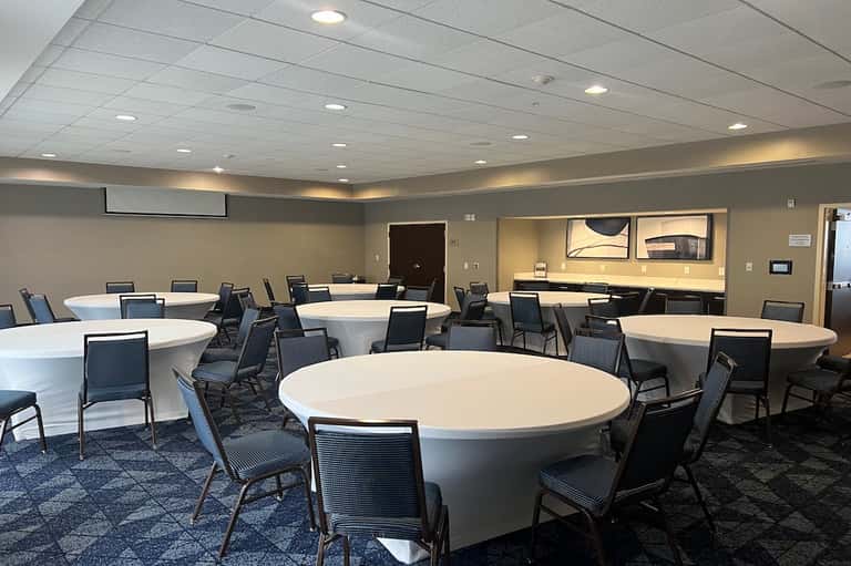 Modern conference room with round white tables, black chairs, recessed lighting, and kitchenette