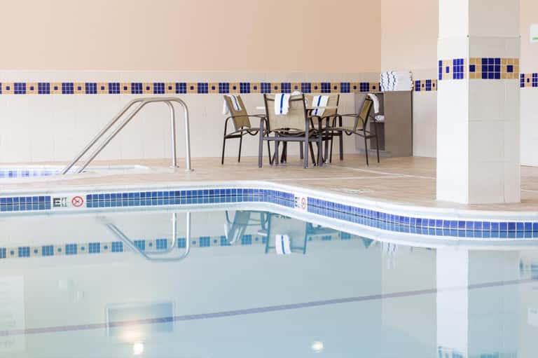 Indoor pool with blue tile border, lounge chairs, and modern seating area