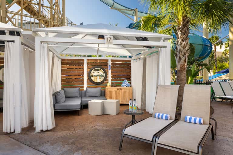 White pergola cabana with seating area and lounge chairs on sandy beach resort deck