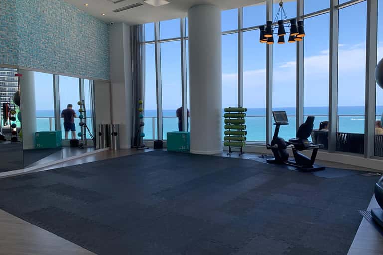 Fitness center with ocean view windows, exercise equipment, and mirrors overlooking turquoise water
