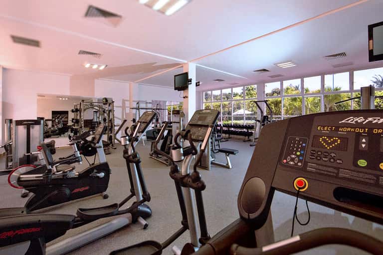 Fitness center with cardio equipment, treadmills, and floor-to-ceiling windows overlooking palm trees