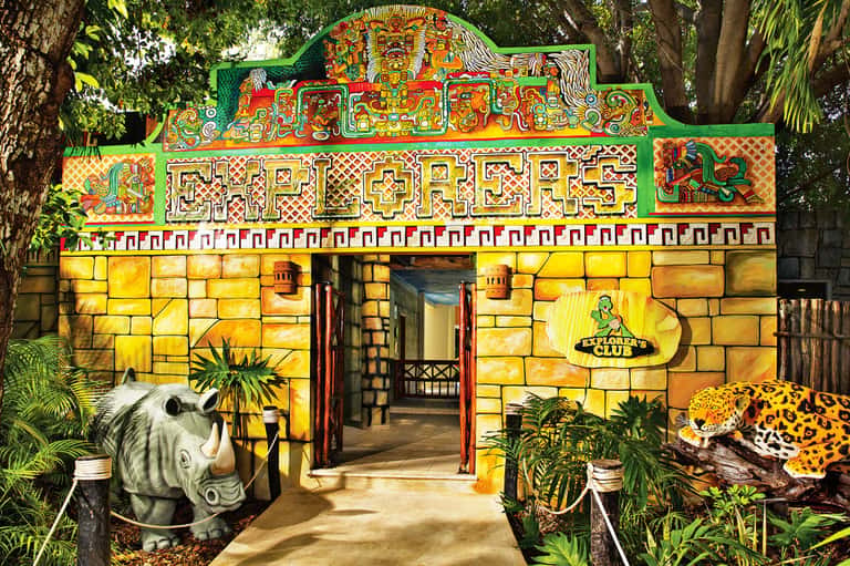 Colorful Mayan-themed entrance with yellow stone facade, decorative animal sculptures and jungle setting