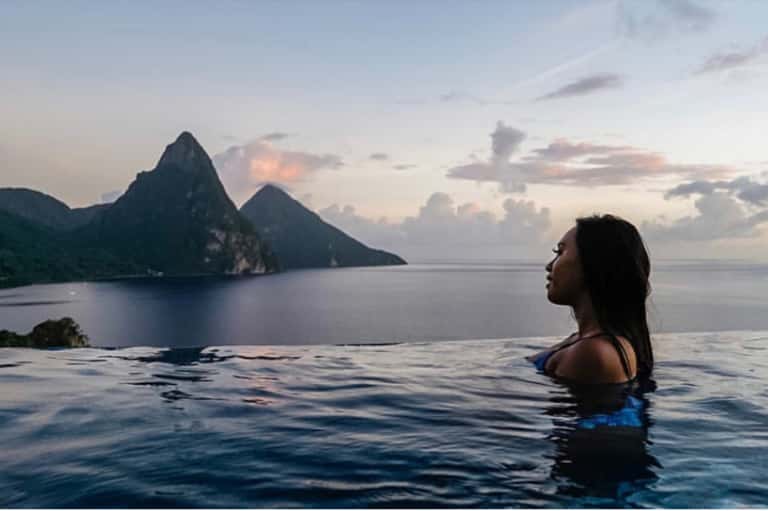 Woman in infinity pool overlooking dramatic mountain peaks and ocean at dusk