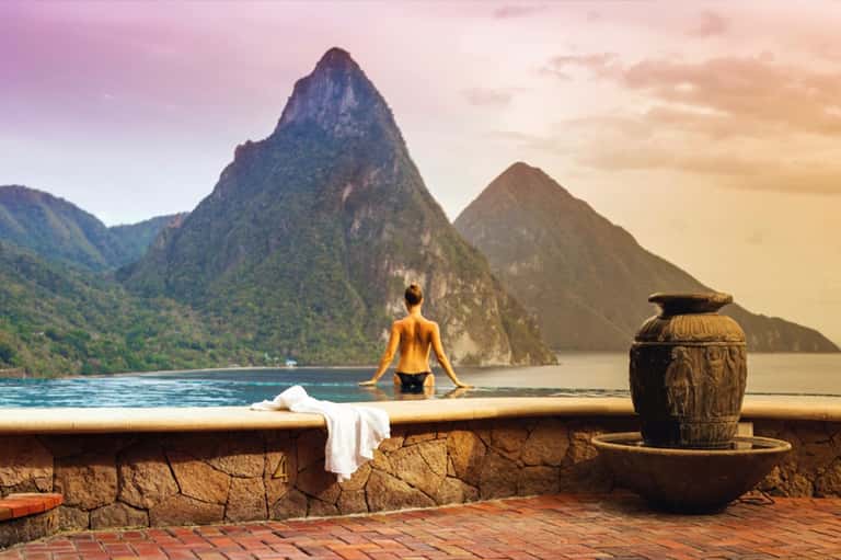 Woman in hot spring pool overlooking dramatic mountain peaks and tropical landscape at golden hour