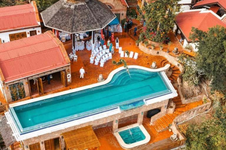 Aerial view of resort with turquoise pool, red-roofed buildings, and ceremony setup