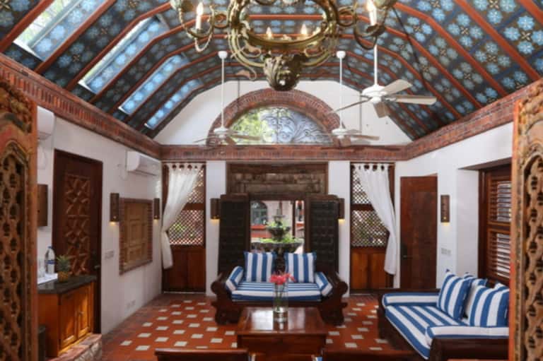 Ornate interior courtyard with decorative ceiling, carved wooden doors, blue striped seating, and traditional tile flooring
