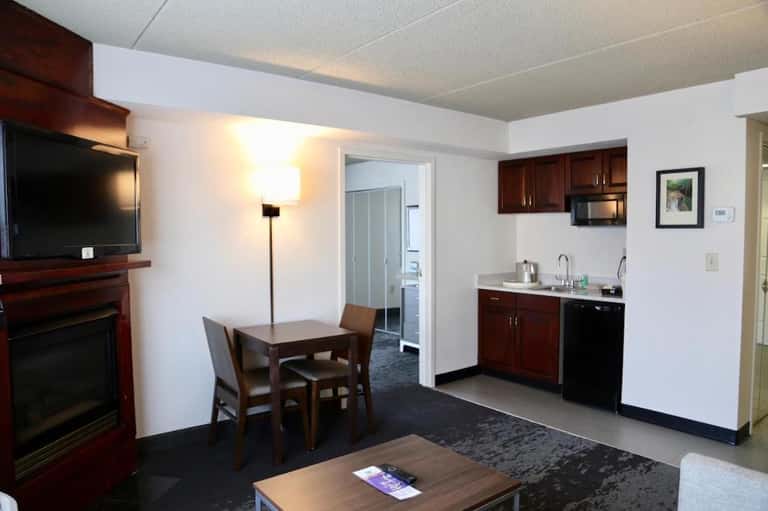 Hotel suite living area with fireplace, kitchenette, dining table, and TV entertainment center