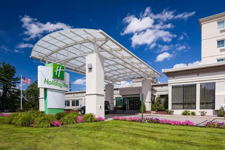 Holiday Inn hotel entrance with green signage, white canopy, and pink flowering landscaping