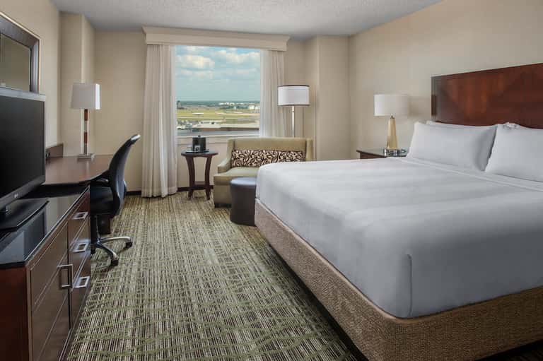 Modern hotel bedroom with queen bed, work desk, and scenic airport view from large window
