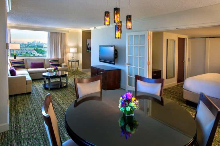 Luxury hotel suite with living area, city skyline views, purple accent pillows, and modern furnishings