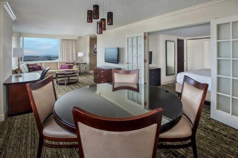 Luxury hotel suite with round dining table, living area, and city skyline view through floor-to-ceiling windows