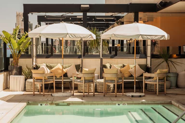 Rooftop lounge area with white umbrellas, seating, and infinity pool