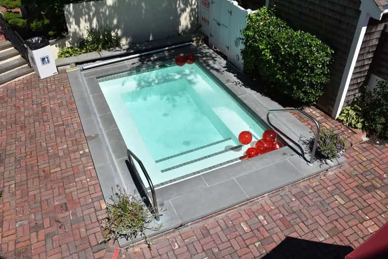 Compact rectangular swimming pool surrounded by brick patio and ivy-covered walls