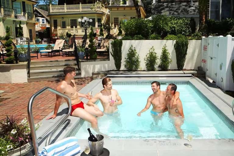 Four men enjoying a resort pool with historic yellow mansion and brick courtyard in background