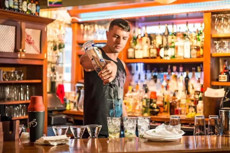 Bartender preparing cocktails at vibrant orange bar with backlit shelving and spirits display