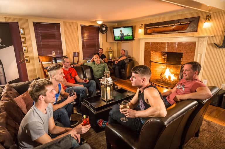 Men relaxing in fireplace lounge with leather seating, TV, and warm ambient lighting