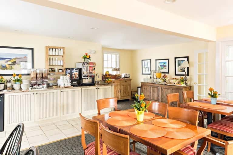 Bright hotel kitchen and dining area with wooden cabinets, dining table, and coastal artwork