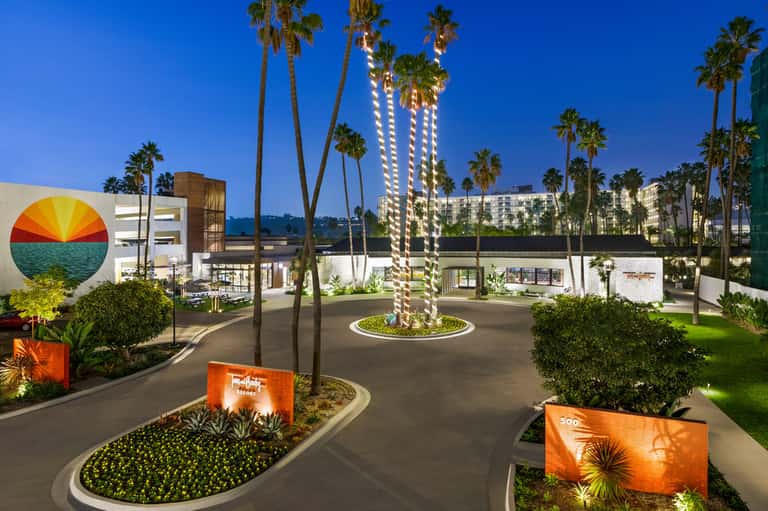 Resort entrance at dusk with illuminated palm trees and colorful sunset artwork
