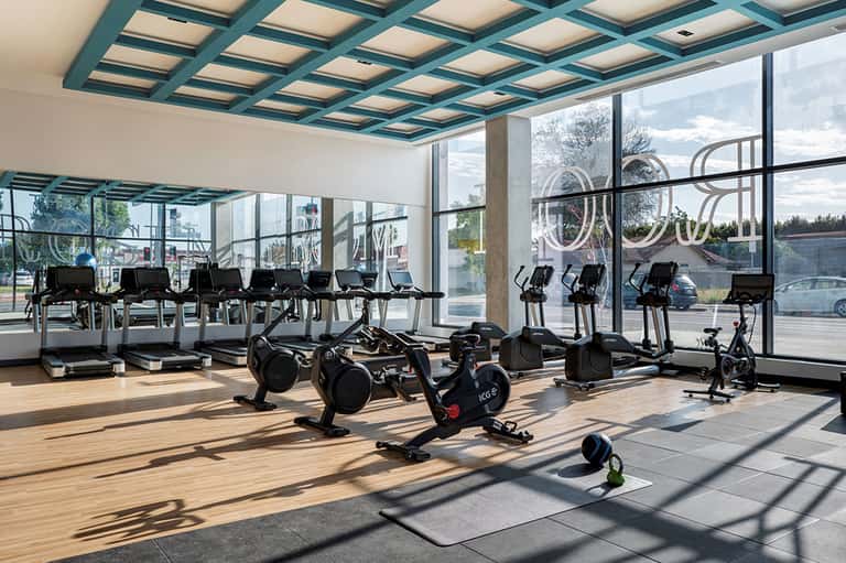 Bright fitness center with exercise bikes, treadmills, and floor-to-ceiling windows with city views
