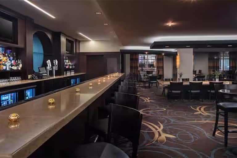 Upscale hotel bar and lounge with long counter, dark wood accents, and modern lighting