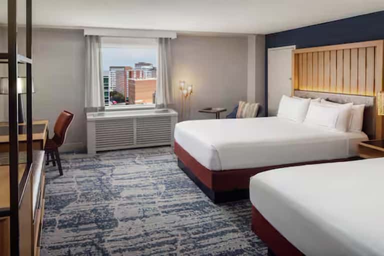 Modern hotel bedroom with two queen beds, navy accent wall, window view, and contemporary furnishings
