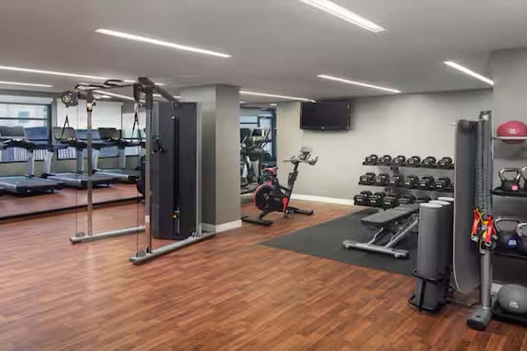 Bright gym interior with wooden flooring, weights, stationary bike, and mirrored wall