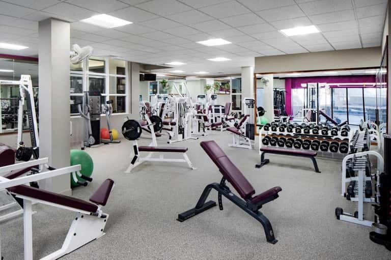Spacious fitness center with weight machines, dumbbells, exercise benches, and large windows