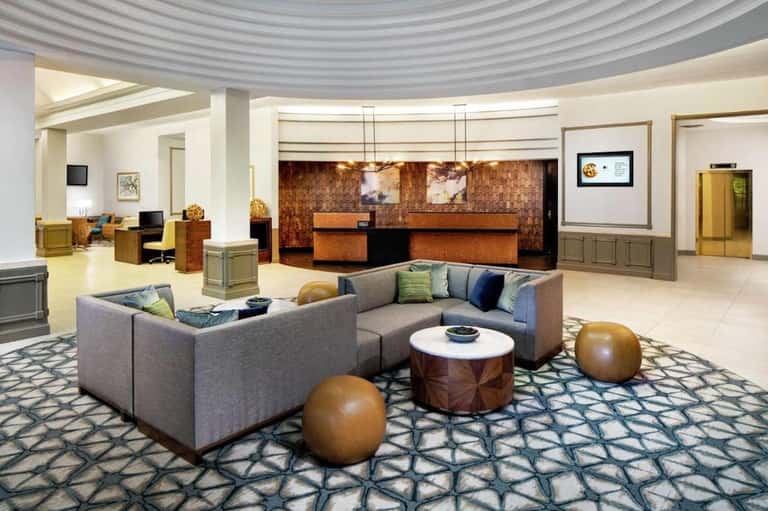 Upscale hotel lobby with curved seating, brass accents, patterned carpet, and reception desk