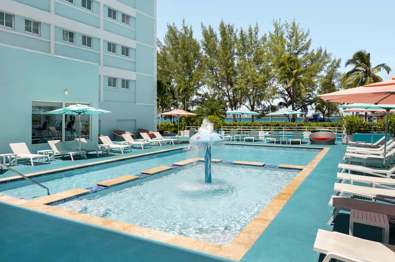 Modern hotel pool with fountain, lounge chairs, umbrellas, and aqua-colored water