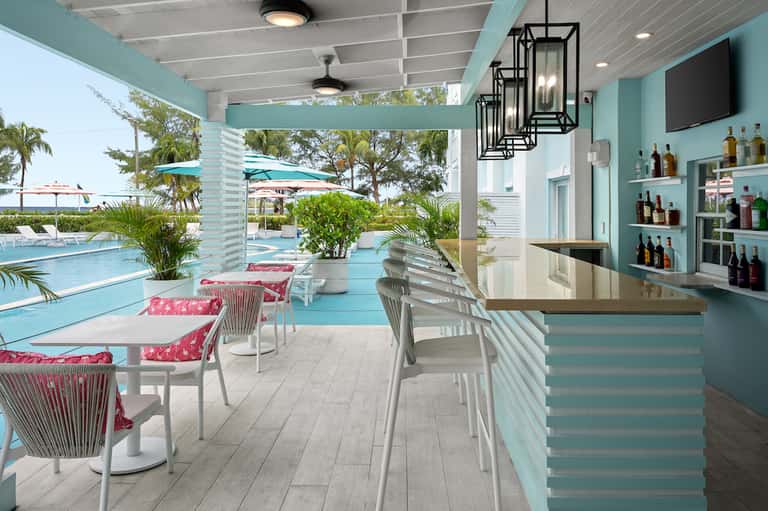 Poolside bar with turquoise accent walls, bar seating, and view of pool and umbrella