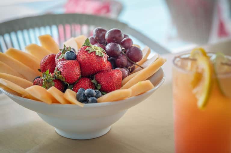 Fresh fruit platter with strawberries, blueberries, grapes, and melon slices beside a citrus beverage