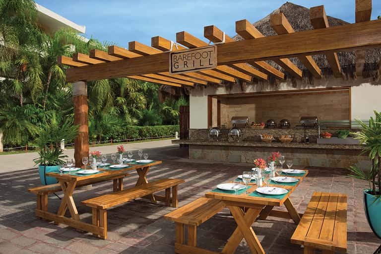 Barefoot Grill outdoor dining area with wooden tables, pergola, and built-in grill station