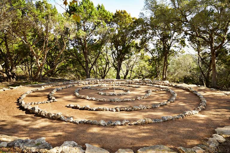 Spiral labyrinth pattern made of white stones on brown earth surrounded by tall trees