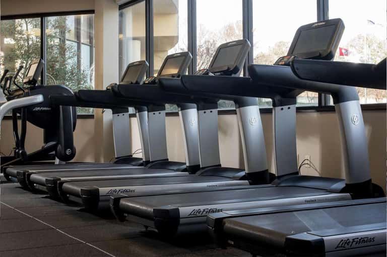 Hotel gym with row of Life Fitness treadmills facing large windows overlooking outdoor landscape