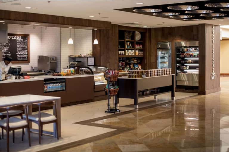 Modern hotel café interior with dark wood finishes, counter service, and refrigerated displays