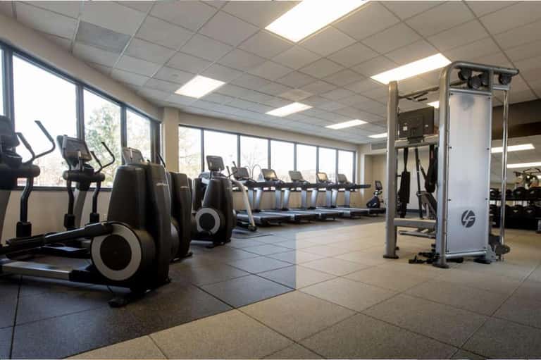 Bright fitness center with cardio equipment, weight machines, and large windows overlooking outdoor landscape