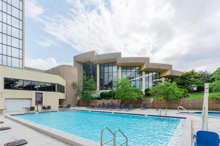 Resort outdoor pool with modern brick building and lounge chairs under cloudy sky