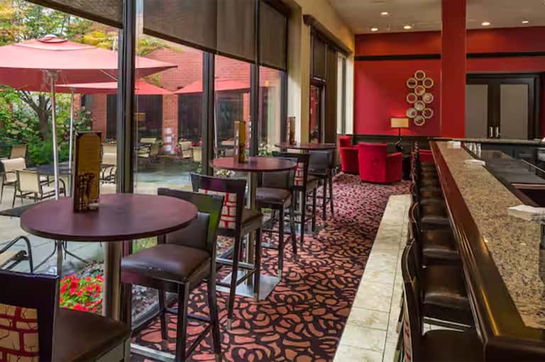 Modern hotel lounge with red accent walls, burgundy seating, patterned carpet, and outdoor patio view