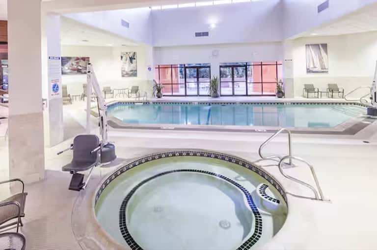 Indoor aquatic facility with indoor pool, hot tub, and spa chairs under skylights