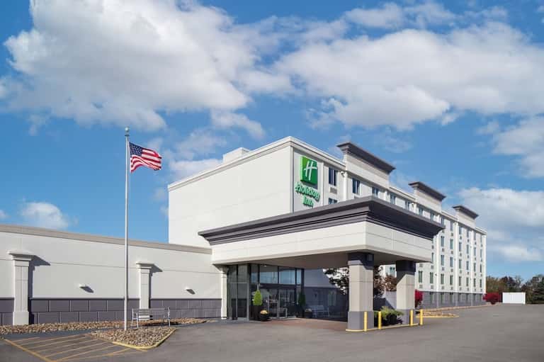 Holiday Inn hotel exterior with white facade, American flag, and parked cars