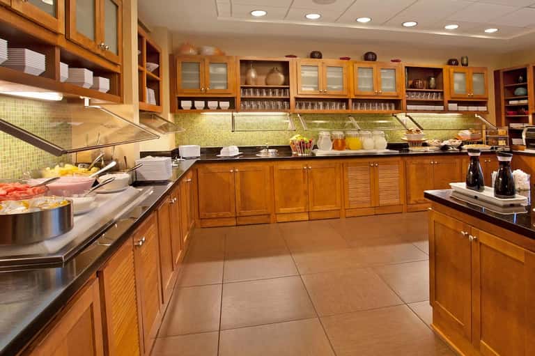 Large hotel kitchen with golden wood cabinetry, green tile backsplash, stainless steel appliances, and full food service setup