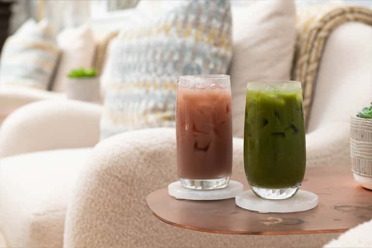 Two iced beverages on a wooden table with cream-colored furniture in a bright lounge area