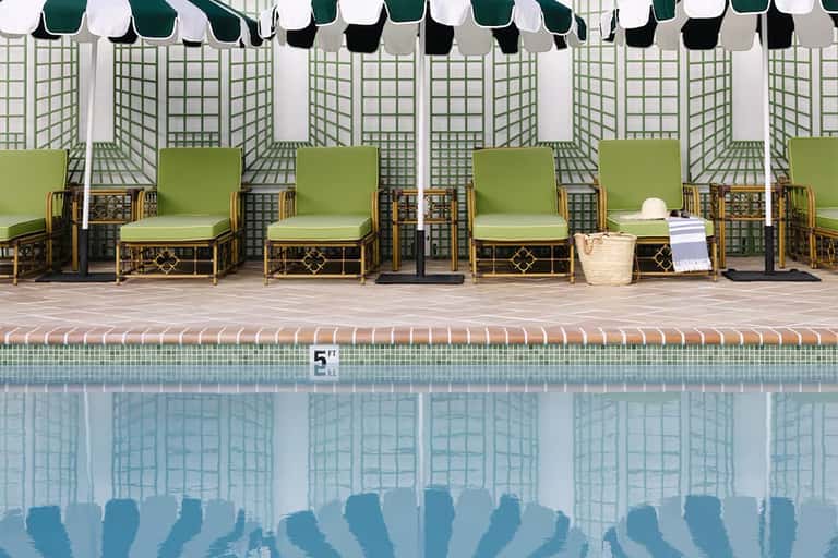 Resort pool with green lounge chairs under striped umbrellas and lattice privacy screens