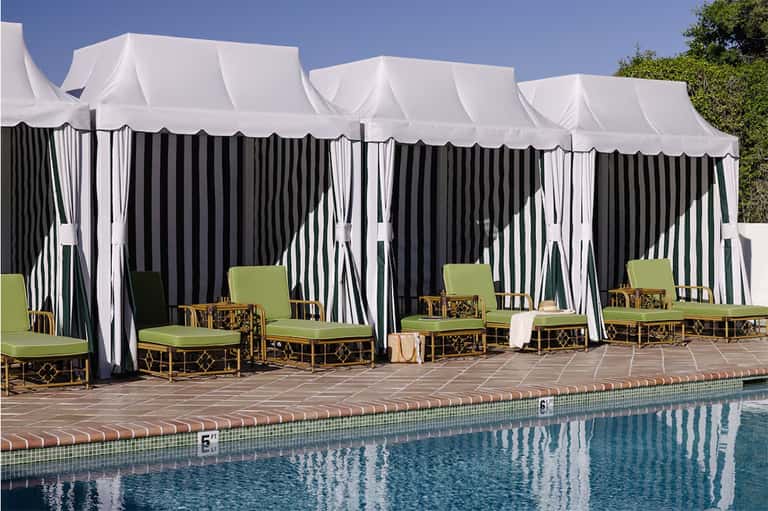 Elegant poolside cabanas with white and black striped curtains, green cushioned seating, and pool view