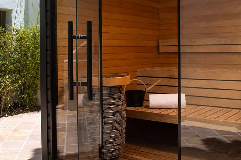 Modern spa sauna interior with wooden walls, glass door, stone heater, and rolled towels
