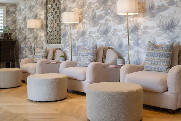 Upscale lounge area with curved cream furniture, patterned wallpaper, floor lamps, and botanical accents