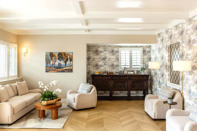 Elegant living room with cream sofa, modern chairs, dark sideboard, patterned wallpaper, herringbone flooring